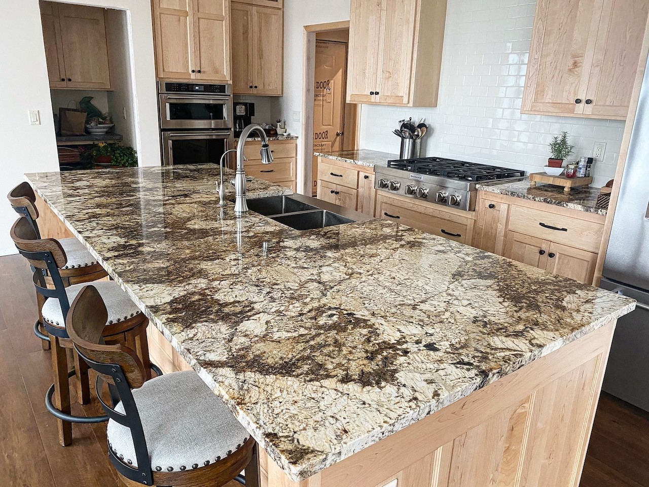 A kitchen with custom designed light wood cabinets, custom granite counter tops and stools.